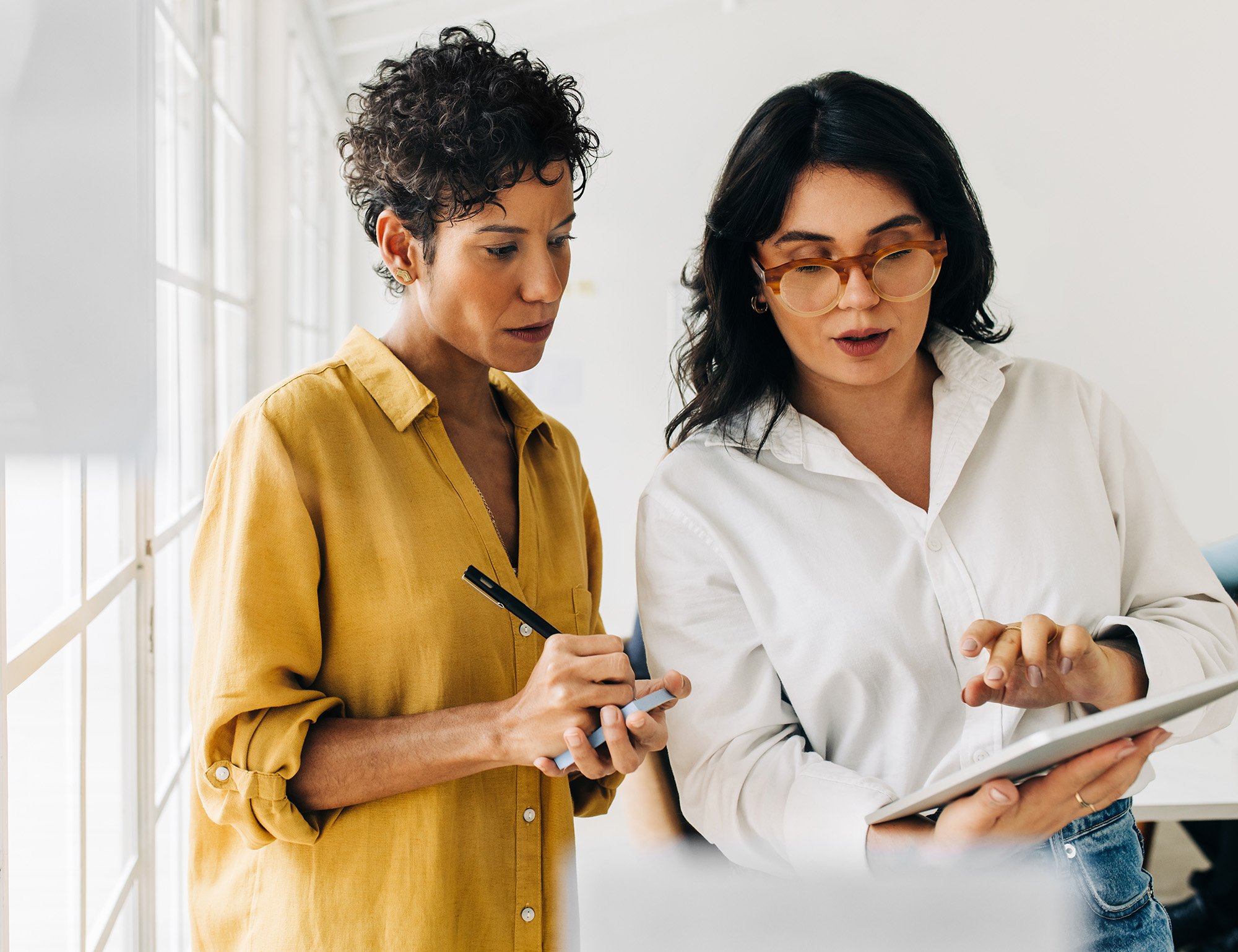 Two women looking at tablet one is taking notes